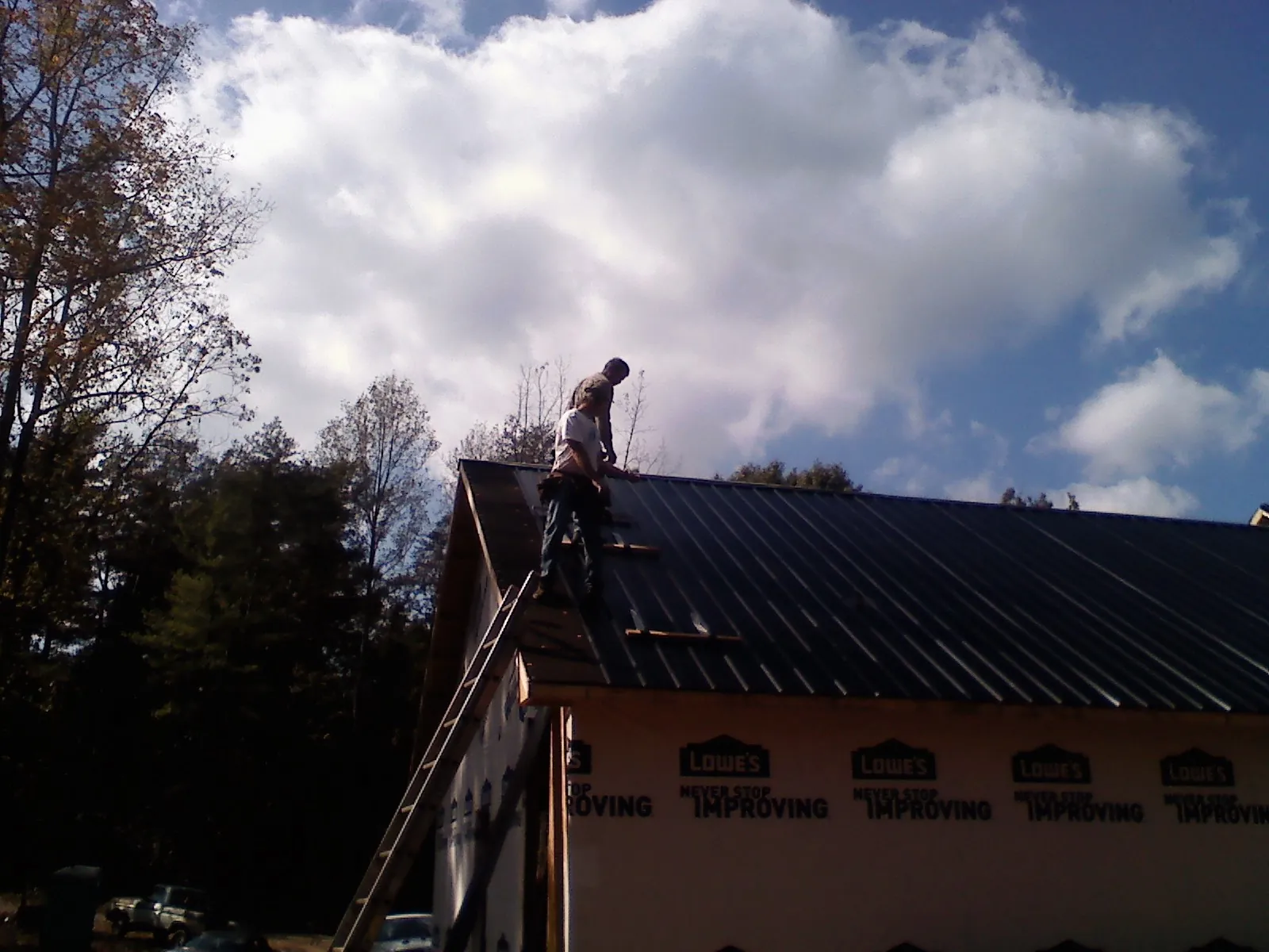 Roofer fastening dark metal panels high against a cloudy sky, from a Roof Inspection job in Williamsport